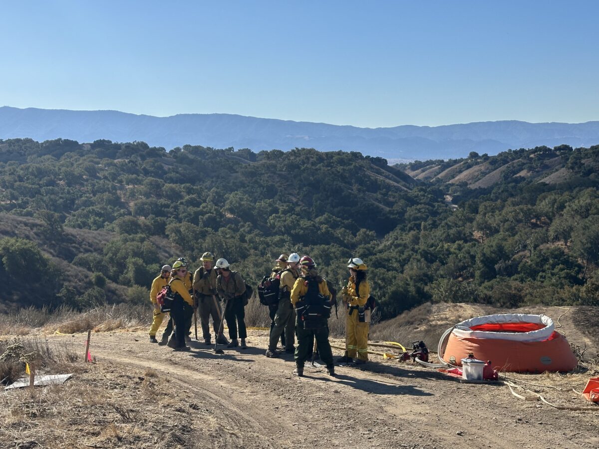 People standing on hill in yellow fire protective clothes next to orange water pumpkin storage unit